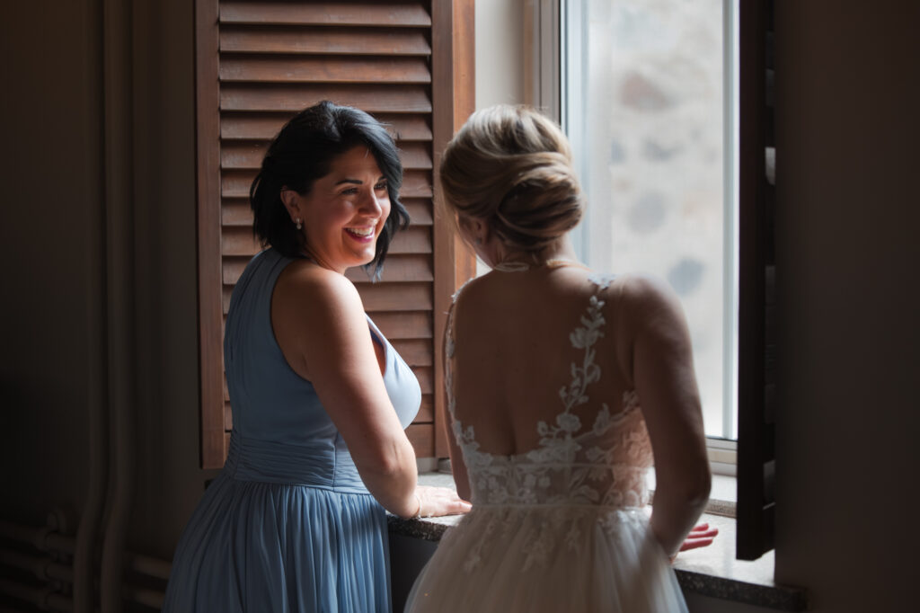Complicité de la mariée avec sa demoiselle d'honneur dans les couloirs de l'Abbaye d'Oka - Éclairage en lumière naturelle - BlanchePhotographe
