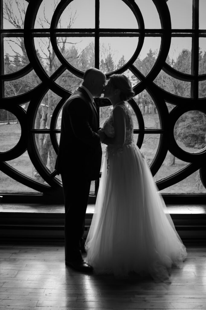 Couple de jeunes mariés en contre-jour devant la rosace de l'Abbaye d'Oka - Photo de mariage en noir et blanc - BlanchePhotographe